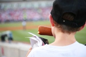 Kid eating a corndog at a ballgame after purchasing it from a custom food cart