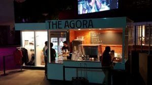 Crowds gather at mobile food cart and bar kiosk on sloped ground at the Greek Theater